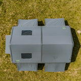 A gray modular pop-up tent or shelter with multiple rectangular sections and small window panels, photographed from above on a grassy field.
