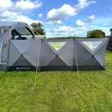 Photo of 3 panels of holawild blackthorn 4.0 poled windbreak being used on grassy campsite with blue sky.