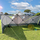Photo of back of holawild blackthorn 4.0 windbreak being used whilst camping on grassy campsite with blue sky and large tunnel tent in background.