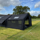 Black tent with mesh sides on a grassy field under a blue sky with clouds. Machu Picchu Shelter Tent in Black.